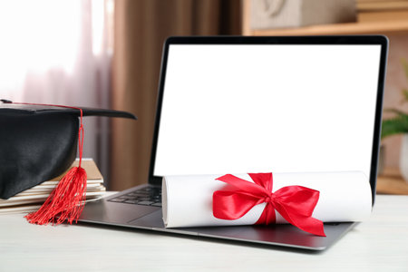 Diploma, graduation cap, stacked copybooks and laptop on white wooden table indoors, closeupの写真素材