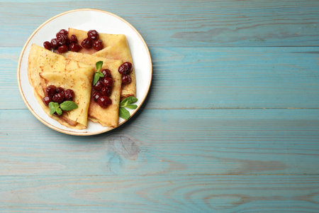 Crepes served with cherry jam on light blue wooden table, top view. Space for text