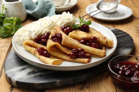 Tasty crepes with cherries, whipped cream and mint served on wooden table, closeupの写真素材