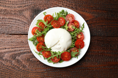 Delicious burrata cheese with arugula and tomatoes on wooden table, top viewの写真素材