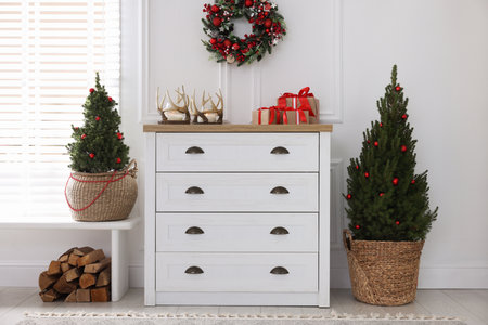 Stylish room with cabinet, small spruce trees and Christmas decor. Interior design