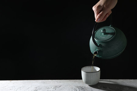 Woman pouring hot tea into cup from teapot at gray table, closeup. Space for textの写真素材