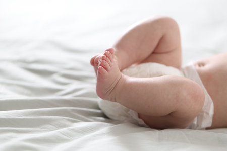 Cute newborn baby in diaper lying on bed indoors, closeup. Space for text