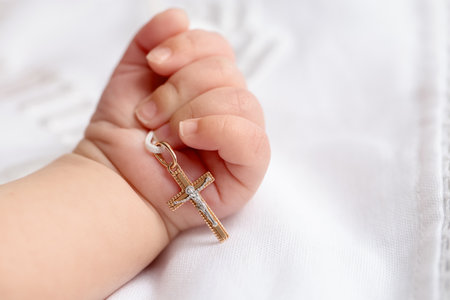 Sacrament of baptism. Little baby holding gold cross on bed, closeupの写真素材