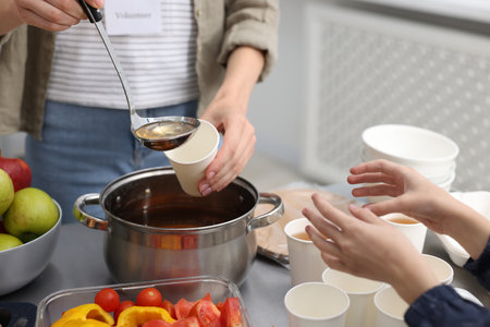 Volunteer giving drink to homeless girl in shelter, closeupの写真素材