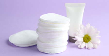 Stack of clean cotton pads, cream and flower on lilac background, closeupの写真素材