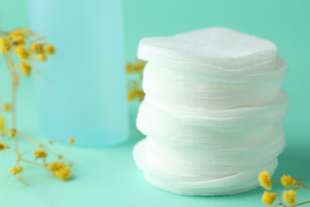 Stack of clean cotton pads and flowers on turquoise background, closeup. Space for textの写真素材