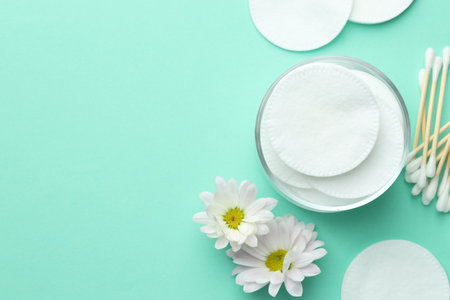 Clean cotton pads, swabs and flowers on turquoise background, flat lay. Space for textの写真素材