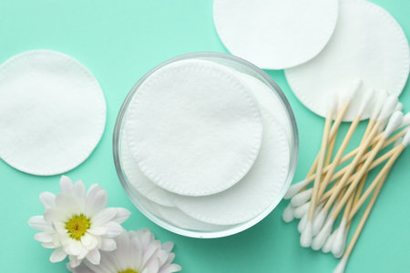 Clean cotton pads, swabs and flowers on turquoise background, flat layの写真素材