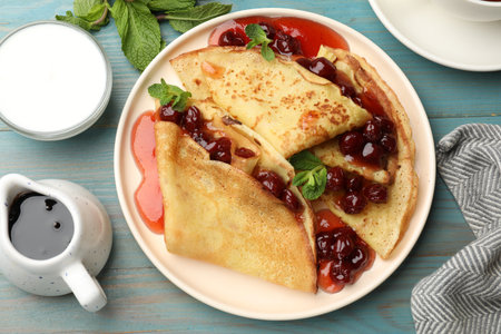Delicious crepes with cherry jam served on light wooden table, flat layの写真素材
