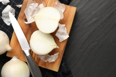 Fresh onion bulbs with peels and knife on black textured table, flat lay. Space for textの写真素材