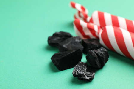 Christmas tradition for kids. Pieces of black coal and candies on green background, closeup. Space...