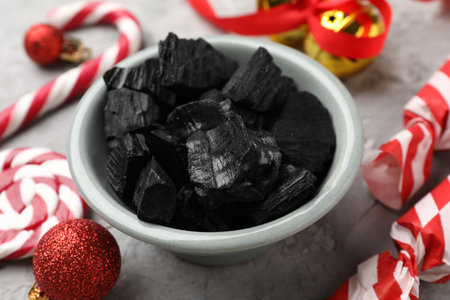 Pieces of black coal in bowl, treats and Christmas decor on gray textured table, closeupの写真素材