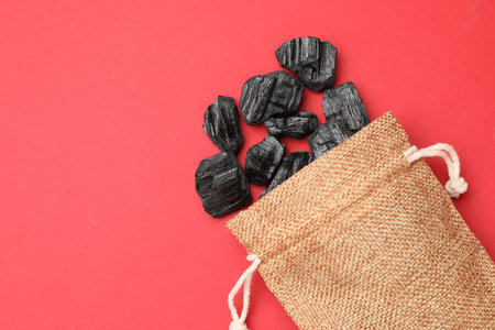 Pieces of black coal in bag on red background, top view. Space for textの写真素材