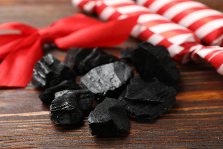 Pieces of black coal, candies and red bow on wooden table, closeup. Christmas tradition for kidsの写真素材