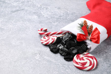 Pieces of black coal, lollipops and candy cane in Christmas stocking on gray textured table, closeup. Space for textの写真素材