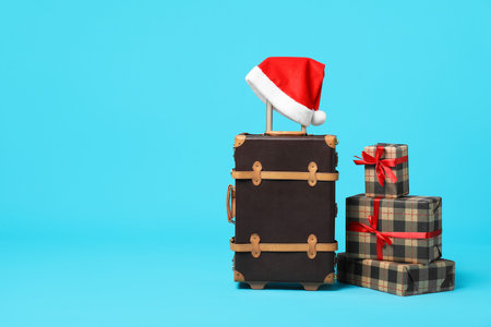 Christmas vacation. Stylish suitcase, Santa hat and gift boxes on light blue background. Space for textの写真素材