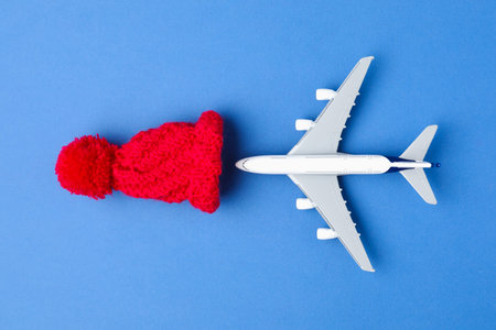 Christmas vacation. Toy plane and hat on blue background, flat lay