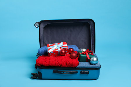 Christmas vacation. Open suitcase with clothes, gift boxes and baubles on light blue backgroundの写真素材