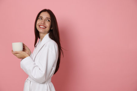 Woman in bathrobe with cup of coffee on pink background. Space for textの写真素材