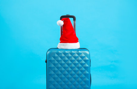 Santa hat on suitcase against light blue background. Christmas vacationの写真素材