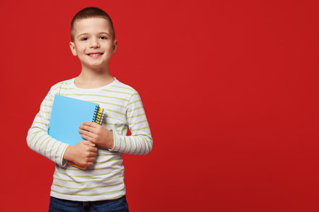 Cute little boy with notebooks on red background, space for text
