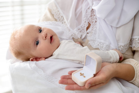 Sacrament of baptism. Woman holding little baby and box with gold cross indoors, closeup