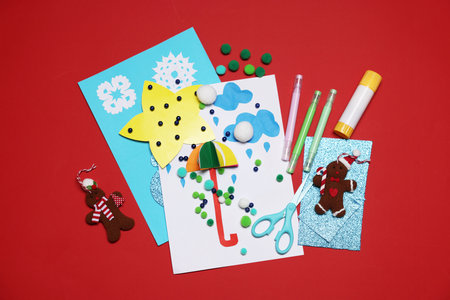 Christmas postcards and handicraft materials on red background, flat lay. Child handmade craft