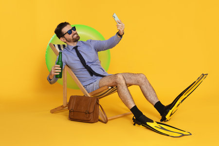 Man with bottle having video chat via smartphone in deck chair on orange backgroundの写真素材