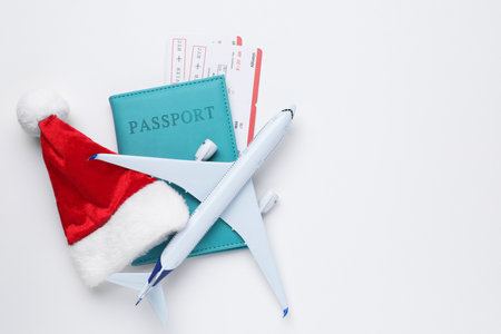 Christmas vacation. Passport with tickets, plane model and Santa hat on white background, flat lay. Space for textの写真素材