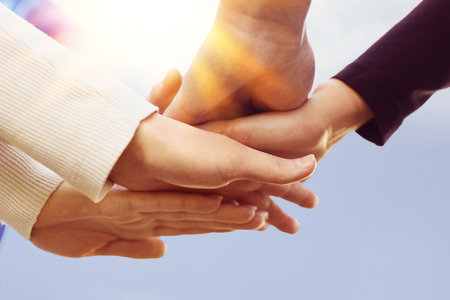 Group of volunteers stacking hands on sunny day, closeup