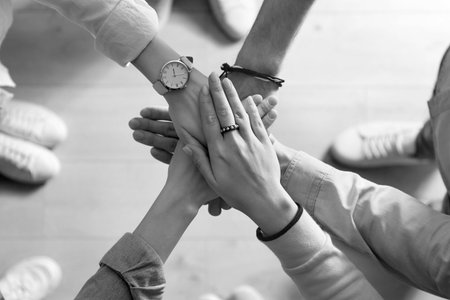 Group of people stacking their hands together, top view. Black-and-white toning