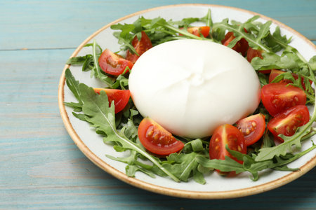 Delicious burrata cheese with tomatoes and arugula on light blue wooden table, closeupの写真素材