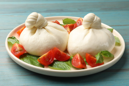 Delicious burrata cheese with tomatoes and basil on light blue wooden table, closeup