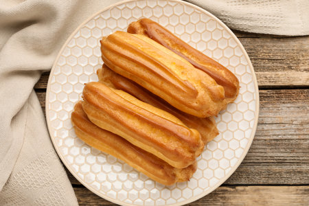 Fresh tasty eclairs on wooden table, top view
