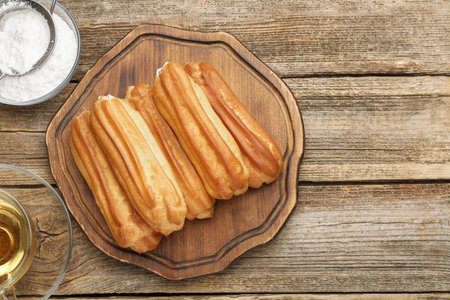 Tasty eclairs, powdered sugar and tea on wooden table, flat lay. Space for textの写真素材
