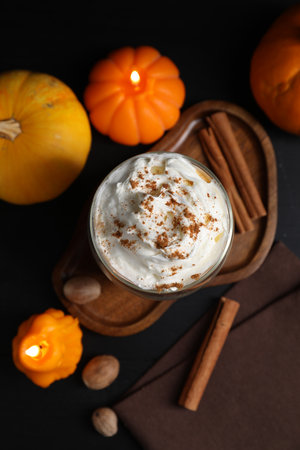 Delicious pumpkin latte with whipped cream and autumn decor on black table, flat layの写真素材