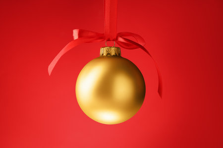 One Christmas ball with bow hanging against red background, closeupの写真素材