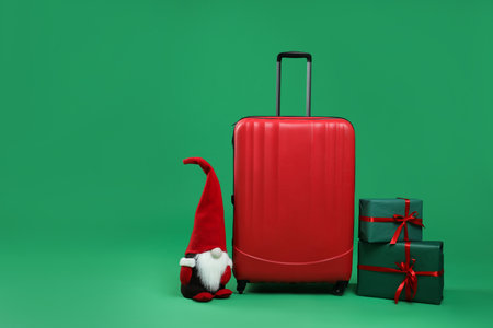 Christmas vacation. Stylish suitcase, gift boxes and decorative gnome on green background. Space for textの写真素材