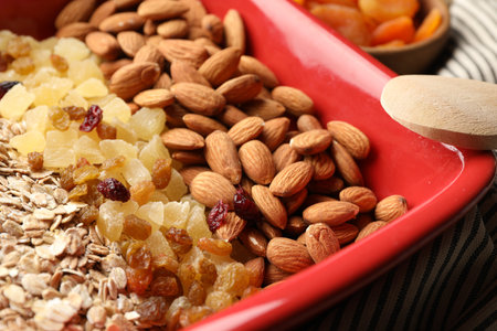 Making granola. Oat flakes, dried fruits and almond nuts in baking dish on table, closeupの写真素材