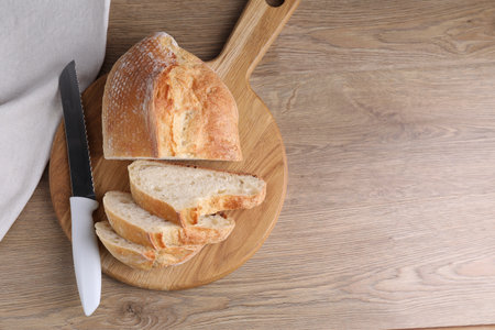 Cut fresh bread and knife on wooden table, top view. Space for textの写真素材