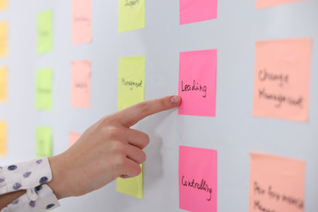 Woman pointing at sticky note with word Leading near whiteboard in office, closeupの写真素材