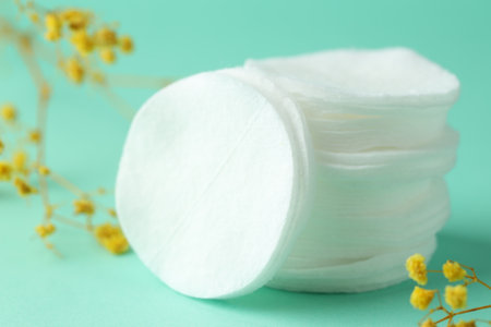 Stack of clean cotton pads and flowers on turquoise background, closeupの写真素材