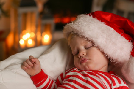 Baby in Christmas pajamas and Santa hat sleeping on bed indoorsの写真素材