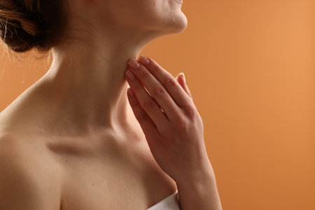 Woman touching her neck on pale orange background, closeup. Space for textの写真素材
