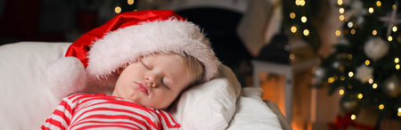 Baby in Christmas pajamas and Santa hat sleeping on bed indoors. Space for textの写真素材