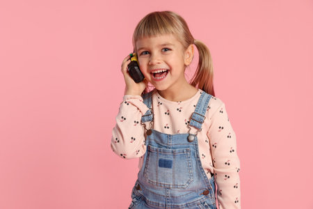 Happy little girl using radio on pink background. Space for text