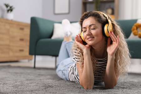 Woman in headphones listening music on floor at home. Space for textの写真素材