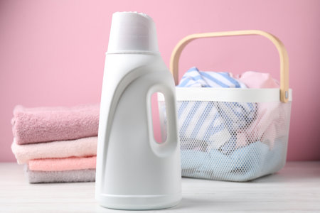Basket with laundry and bottle of detergent on white wooden table against pink background, closeupの写真素材