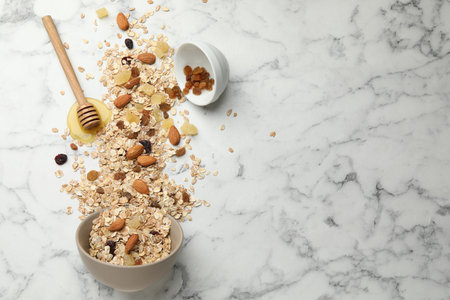 Making granola. Flat lay composition with oat flakes, dried fruits, almond nuts and honey on white marble table. Space for textの写真素材